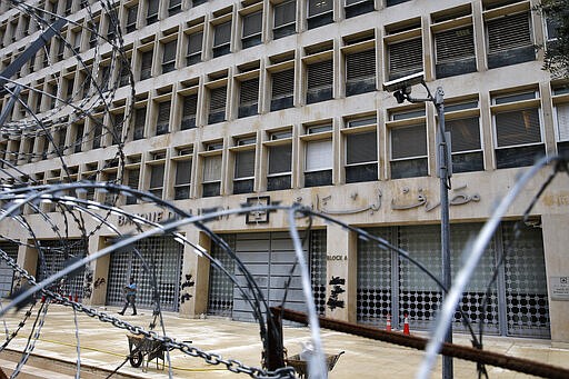 In this Wednesday, March 18, 2020 photo, a worker walks outside the Lebanese Central Bank that has been shut down as part of the preventive measures against the coronavirus, in Beirut, Lebanon. The COVID-19 pandemic has managed to do what various wars could not: Close bars, restaurants and entertainment spots across the tiny Mediterranean country. It's another economic gut punch, delivered at a time when Lebanon is mired in the worst financial crisis in its history -- one that could hasten the country's long-feared economic collapse. (AP Photo/Bilal Hussein)