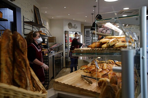 Bakers sell bread in a Boulogne Billancourt bakery, outside Paris, Tuesday, March 24, 2020. French President Emmanuel Macron urged employees to keep working in supermarkets, production sites and other businesses that need to keep running amid stringent restrictions of movement due to the rapid spreading of the new coronavirus in the country. For most people, the new coronavirus causes only mild or moderate symptoms. For some it can cause more severe illness, especially in older adults and people with existing health problems. (AP Photo/Christophe Ena)