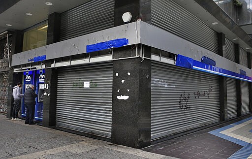 In this Wednesday, March 18, 2020 photo, people use an ATM outside a bank that has been shut down as part of the preventive measures against the coronavirus, in Beirut, Lebanon. COVID-19 has managed to do what various wars could not: Close bars, restaurants and entertainment spots across the tiny Mediterranean country. It's another economic gut punch, delivered at a time when Lebanon is mired in the worst financial crisis in its history -- one that could hasten the country's long-feared economic collapse. (AP Photo/Bilal Hussein)