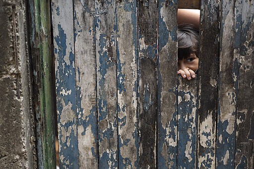 A boy peaks from the dilapidated doorway of his home as his mother receives soap and detergent distributed by volunteers as an effort to avoid the spread of the new coronavirus, in the Rocinha slum of Rio de Janeiro, Brazil, Tuesday, March 24, 2020. (AP Photo/Leo Correa)