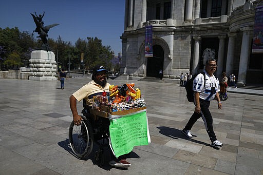 Guillermo Gonzalez Sanchez sells cigarettes and snacks from atop his wheelchair, outside the Palace of Fine Arts in downtown Mexico City, Tuesday, March 24, 2020. Gonzalez, who doesn't believe the new coronavirus is real, says the threat is just the latest tactic to suppress the Mexican people, many of whom like him live from day to day. (AP Photo/Rebecca Blackwell)