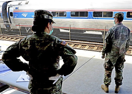 Members of the 1207th Rhode Island National Guard unit stand at the Westerly, R.I., Amtrak station Friday, March 27, 2020, to inform passengers from New York of the 14-day quarantine restrictions if disembarking in Rhode Island ordered by Gov. Gina Raimondo. At the time of the photo, no passengers had disembarked at the station. (Harold Hanka/The Sun via AP)