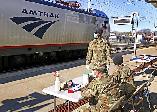 Members of the 1207th Rhode Island National Guard wait for disembarking passengers at the Amtrak station in Westerly, R.I., Friday, March 27, 2020, to inform passengers from New York of the 14-day quarantine restrictions if disembarking in Rhode Island ordered by Gov. Gina Raimondo. No passengers had disembarked at the time of the photo. (Harold Hanka/The Sun via AP)