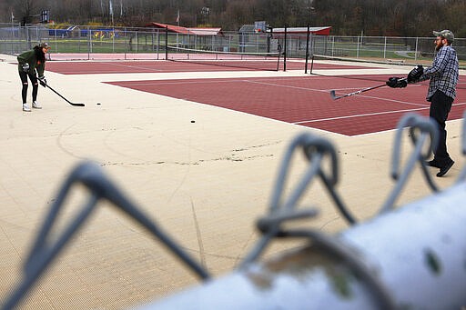 Jason Dapper, right, passes a puck to his wife Lexi Dapper as the two use the tennis courts at the local park to practice their hockey skills, Friday, March 27, 2020, in Zelienople, Pa. The couple said they have taken to the park since the local rinks have closed with the outbreak of COVID-19. (AP Photo/Keith Srakocic)