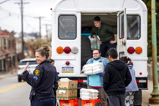 Pittsburgh Police Officer Tiffany Kline-Costa stops traffic as volunteers unload meals from a decommissioned school bus on Friday, March 27, 2020, at a bus stop in the Mt. Oliver neighborhood of Pittsburgh. Local nonprofits 412 Food Rescue, A+ Schools and the Latino Community Center created a pilot meal-delivery program supported by Pittsburgh-area native and actor Michael Keaton during the COVID-19 pandemic, serving more than 500 meals prepared by local restaurants Bar Botanico, The Vandal and DiAnoia's Eatery. (Steph Chambers/Pittsburgh Post-Gazette via AP)