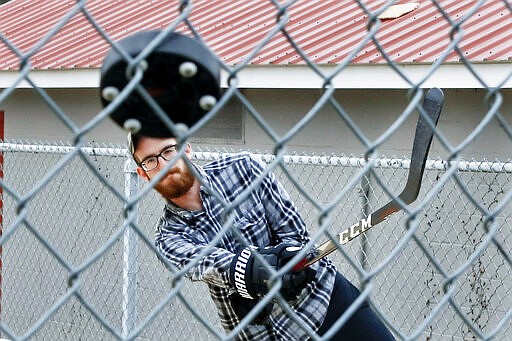 Jason Dapper, shoots a street hockey puck at the fence in one of the tennis courts at the local park as he practices his hockey skills with his wife, Friday, March 27, 2020, in Zelienople, Pa. The couple said they have taken to the park since the local rinks have closed with the outbreak of COVID-19. (AP Photo/Keith Srakocic)