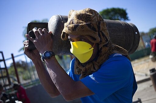 A man wearing homemade face protection carries a full cylinder of cooking gas after waiting in a long line for the gas truck to arrive during a lockdown to contain the spread of the new coronavirus in Caracas, Venezuela, Friday, March 27, 2020. (AP Photo/Ariana Cubillos)