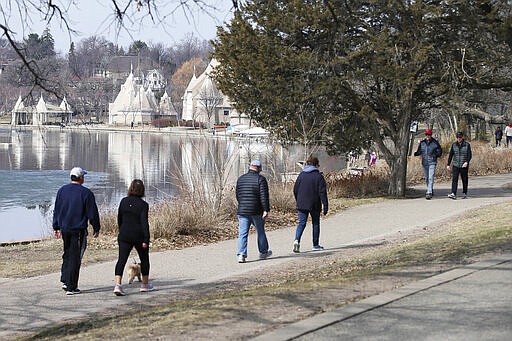 Walkers take advantage of a spring day Friday, March 27, 2020 at Lake Harriet in Minneapolis. Minnesota Gov. Tim Walz issued a stay-at-home order effective at midnight Friday to help stop the spread of the coronavirus in the state. Outdoor activities such as walking are permitted. The new coronavirus causes mild or moderate symptoms for most people, but for some, especially older adults and people with existing health problems, it can cause more severe illness or death. (AP Photo/Jim Mone)