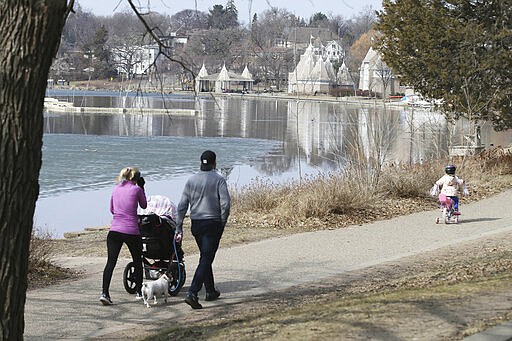 A family takes a walk around Lake Harriet as a Canada goose family, center right, enjoys the open water Friday, March 27, 2020, in Minneapolis. Gov. Tim Walz issued a stay-at-home order effective at midnight Friday to help stop the spread of the coronavirus in the state. Walz's order calls on Minnesotans who work in nonessential jobs to stay home when possible for two weeks, though they may go out for essential needs such as trips to the supermarket and pharmacy, doctor visits and for outdoor recreation if they practice social distancing.  (AP Photo/Jim Mone)