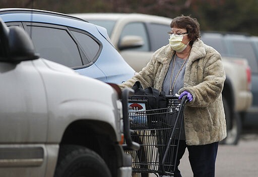 A shopper wears a surgical mask while pushing her purchases to her vehicle outside a Safeway grocery store during a statewide stay-at-home order in an effort to reduce the spread of the new coronavirus Friday, March 27, 2020, in Evergreen, Colo. The new coronavirus causes mild or moderate symptoms for most people, but for some, especially older adults and people with existing health problems, it can cause more severe illness or death. (AP Photo/David Zalubowski)