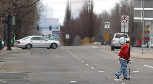 A lone pedestrian crosses a nearly-empty South Broadway during a statewide stay-at-home order in an effort to reduce the spread of the new coronavirus, Friday, March 27, 2020, in Englewood, Colo. The new coronavirus causes mild or moderate symptoms for most people, but for some, especially older adults and people with existing health problems, it can cause more severe illness or death.  (AP Photo/David Zalubowski)