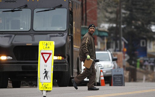 A United Parcel Service delivery driver checks for traffic while crossing the nearly-empty main street during a statewide stay-at-home order in an effort to reduce the spread of the new coronavirus Friday, March 27, 2020, in Evergreen, Colo. The new coronavirus causes mild or moderate symptoms for most people, but for some, especially older adults and people with existing health problems, it can cause more severe illness or death. (AP Photo/David Zalubowski)