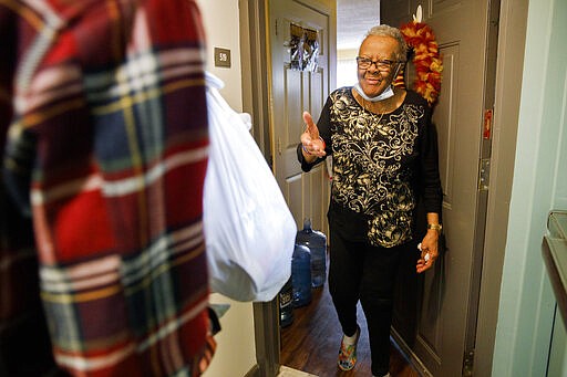 Easter Brown, 77, of Washington, greets Michael Weber, with the nonprofit organization &quot;We Are Family DC,&quot; as he delivers groceries to her apartment door, Saturday, March 21, 2020, in Washington. Seniors are being encouraged to stay in their homes due to the risk of the COVID-19 coronavirus. (AP Photo/Jacquelyn Martin)