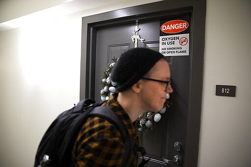 Noel Schroeder, with the nonprofit organization, &quot;We Are Family DC,&quot; walks past a senior's door that warns of oxygen in use, as she delivered groceries to seniors in an apartment building, Saturday, March 21, 2020, in Washington. Seniors are being encouraged to stay in their homes due to the risk of the COVID-19 coronavirus. (AP Photo/Jacquelyn Martin)