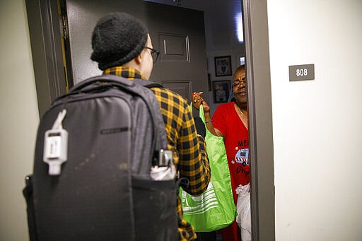 Denise Edmondson, 66, of Washington, right, greets Noel Schroeder, with the nonprofit organization &quot;We Are Family DC,&quot; as she delivered groceries to Edmondson's apartment door, Saturday, March 21, 2020, in Washington. Seniors are being encouraged to stay in their homes due to the risk of the COVID-19 coronavirus. (AP Photo/Jacquelyn Martin)