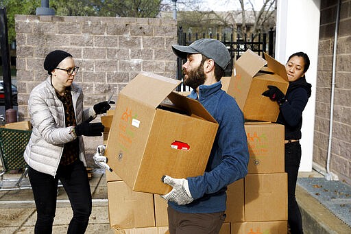 Volunteers with the nonprofit organization &quot;We Are Family DC,&quot; from left, Noel Schroeder, Art Chambers, and Alida Pham, wear cloth gloves due to the lack of available plastic ones as they pack boxes of food to deliver to seniors' homes, Saturday, March 21, 2020, in Washington. Seniors are being encouraged to stay in their homes due to the risk of the COVID-19 coronavirus. (AP Photo/Jacquelyn Martin)