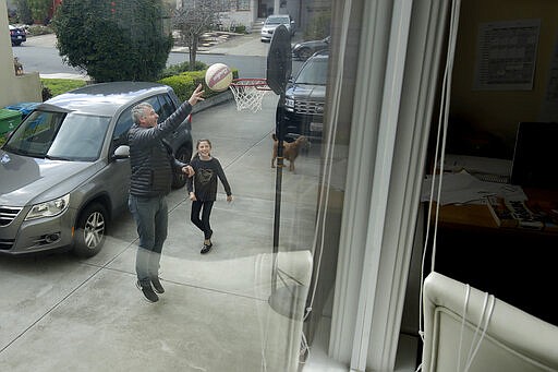 In this Thursday, March 19, 2020, photo, Frankie Keenan shoots baskets with his daughter Rachel, 9, at their home in San Francisco. California's Bay Area has been shut down for more than a week, the first region of America to order its residents to stay home, work remotely and homeschool their children in a desperate bid to slow the spread of the coronavirus pandemic. (AP Photo/Jeff Chiu)