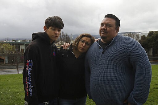 In this Tuesday, March 24, 2020, photo, Ricardo Bautista, 14, from left, poses for photos with his mother, Sonia Bautista, and his father, William Gonzalez, in South San Francisco, Calif. California's Bay Area has been shut down for more than a week, the first region of America to order its residents to stay home, work remotely and homeschool their children in a desperate bid to slow the spread of the coronavirus pandemic. (AP Photo/Jeff Chiu)