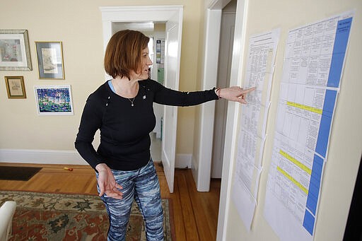 In this Thursday, March 19, 2020, photo, Rebecca Biernat points to a recommended kindergarten daily curriculum schedule for her son Seamus Keenan at their home in San Francisco. California's Bay Area has been shut down for more than a week, the first region of America to order its residents to stay home, work remotely and homeschool their children in a desperate bid to slow the spread of the coronavirus pandemic. (AP Photo/Jeff Chiu)