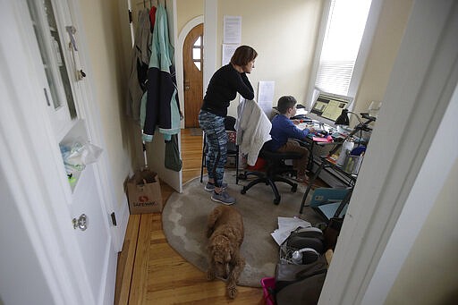 In this Thursday, March 19, 2020, photo, Rebecca Biernat watches as her son Seamus Keenan, 6, takes a live class online at their home in San Francisco. At bottom is their dog, Rosie. California's Bay Area has been shut down for more than a week, the first region of America to order its residents to stay home, work remotely and homeschool their children in a desperate bid to slow the spread of the coronavirus pandemic. (AP Photo/Jeff Chiu)