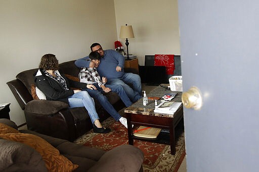 In this Tuesday, March 24, 2020, photo, Sonia Bautista, left, watches as husband William Gonzalez, right, hugs their son Ricardo Bautista, 14, while posing for photos in their apartment in South San Francisco, Calif. California's Bay Area has been shut down for more than a week, the first region of America to order its residents to stay home, work remotely and homeschool their children in a desperate bid to slow the spread of the coronavirus pandemic. (AP Photo/Jeff Chiu)