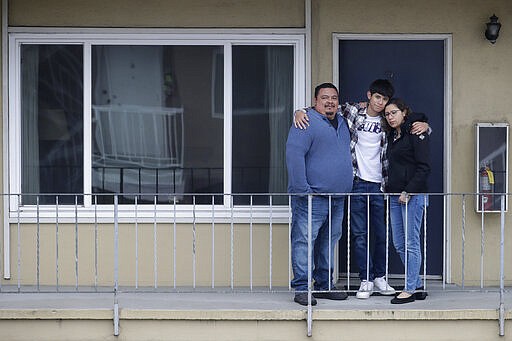 In this Tuesday, March 24, 2020, photo, William Gonzalez, from left, poses for photos with son Ricardo Bautista, 14, and wife, Sonia Bautista, outside of their apartment in South San Francisco, Calif. California's Bay Area has been shut down for more than a week, the first region of America to order its residents to stay home, work remotely and homeschool their children in a desperate bid to slow the spread of the coronavirus pandemic. (AP Photo/Jeff Chiu)