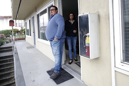 In this Tuesday, March 24, 2020, photo, William Gonzalez, left, and wife Sonia Bautista wait to go for a walk with their son Ricardo Bautista, while being interviewed in South San Francisco, Calif. California's Bay Area has been shut down for more than a week, the first region of America to order its residents to stay home, work remotely and homeschool their children in a desperate bid to slow the spread of the coronavirus pandemic. (AP Photo/Jeff Chiu)