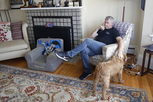 In this Thursday, March 19, 2020, photo, Frankie Keenan pets his family's dog, Rosie, at his home in San Francisco. California's Bay Area has been shut down for more than a week, the first region of America to order its residents to stay home, work remotely and homeschool their children in a desperate bid to slow the spread of the coronavirus pandemic. (AP Photo/Jeff Chiu)