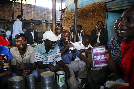 FILE - In this March 22, 2020, file photo, Kenyans gather in a drinking den on the last day such activities will be permitted, in the Kibera slum of Nairobi, Kenya. The new coronavirus causes mild or moderate symptoms for most people, but for some, especially older adults and people with existing health problems, it can cause more severe illness or death. (AP Photo/Brian Inganga, File)