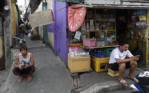 FILE - In this March 24, 2020, file photo, a sign that prohibits non-residents from entering the area is hung at the entrance of a slum area as two men sit outside while the city goes on enhanced community quarantine to prevent the spread of the new coronavirus in Metro Manila, Philippines. The new coronavirus causes mild or moderate symptoms for most people, but for some, especially older adults and people with existing health problems, it can cause more severe illness or death. (AP Photo/Aaron Favila, File)