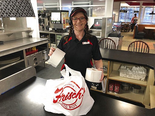 In this photo made on March 20, 2020, Frisch's Big Boy restaurant employee Nicole Cox bags up an order of toilet paper, among in-demand items including milk and bread the double-decker burger chain is now offering during the coronavirus outbreak in Cincinnati, Ohio.  With business sinking under coronavirus outbreak restrictions,the nation's restaurants are transforming operations and menus to try to stay afloat. (AP Photo/Dan Sewell)