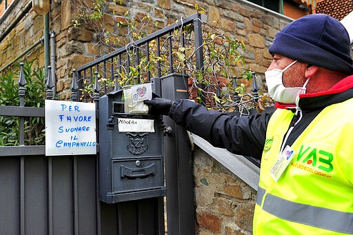 A volunteer delivers a mask to protect against coronavirus in the Tuscan town of Castiglione della Pescaia, Italy, Friday, March 27, 2020. The new coronavirus causes mild or moderate symptoms for most people, but for some, especially older adults and people with existing health problems, it can cause more severe illness or death. Writing at left reads &quot;Please ring the bell&quot; (Jennifer Lorenzini/LaPresse via AP)