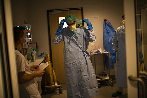 In this photograph taken from behind a window medical personnel work in the intensive care ward for Covid-19 patients at the MontLegia CHC hospital in Liege, Belgium, Friday, March 27, 2020. The new coronavirus causes mild or moderate symptoms for most people, but for some, especially older adults and people with existing health problems, it can cause more severe illness or death. (AP Photo/Francisco Seco)