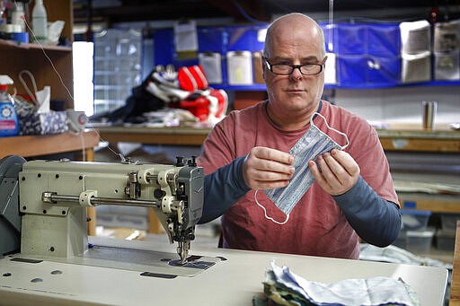 In this Monday, March 23, 2020 photo, Eric Baldwin examines the stitching on a cotton mask, one of hundreds he and the employees at his sail-maintenance business are making for caregivers during the coronavirus outbreak, at his shop in Freeport, Maine. (AP Photo/Robert F. Bukaty)