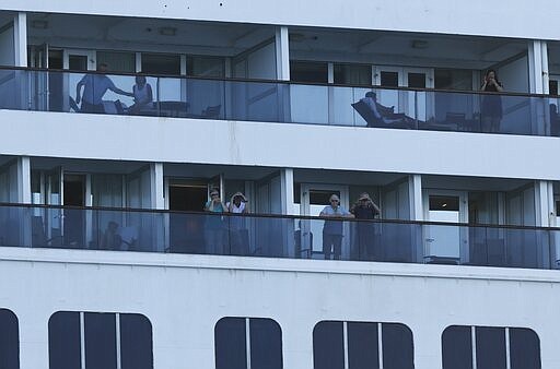 Passengers look out from the Zaandam cruise ship, anchored in the bay of Panama City, Friday, March 27, 2020. Several passengers have died aboard the cruise ship and a few people aboard the ship have tested positive for the new coronavirus, the cruise line said Friday, with hundreds of passengers unsure how long they will remain at sea. (AP Photo/Arnulfo Franco)