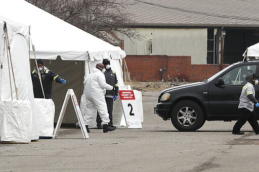 Health care officials watch as a vehicle approaches a testing site at the Michigan State Fairgrounds, Friday, March 27, 2020, in Detroit. The city set up several stations at the fairgrounds to allow for drive up testing for the coronavirus. (AP Photo/Carlos Osorio)