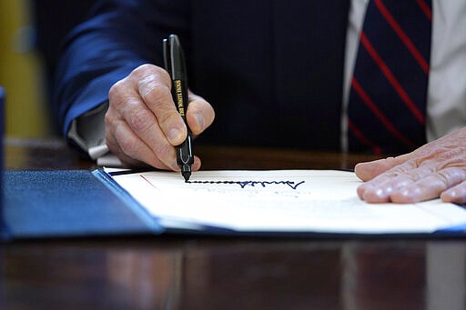 President Donald Trump signs the coronavirus stimulus relief package in the Oval Office at the White House, Friday, March 27, 2020, in Washington. (AP Photo/Evan Vucci)