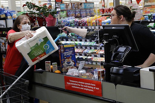 A shopper is separated from a clerk by a plexiglass panel as she checks out at a Hy-Vee grocery store Thursday, March 26, 2020 in Overland Park, Kan. Stores have begun installing the shields in checkout aisles as a precaution to protect clerks and help stop the spread the new coronavirus. (AP Photo/Charlie Riedel)