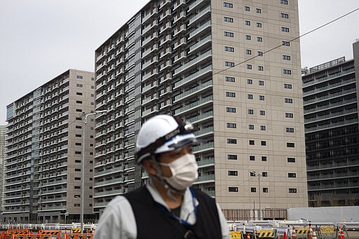 FILE - In this Monday, March 23, 2020, file photo, a masked worker walks through the athletes' village for the Tokyo 2020 Olympics, in Tokyo. The Tokyo Olympics have been moved to next year. The sprawling site on Tokyo Bay - 5,632 apartments - will be sold off after the Olympics. Reports say about one-quarter of the units have already been sold. (AP Photo/Jae C. Hong, File)