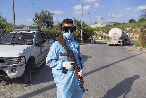 Palestinian policeman mans a checkpoint to receive and register laborers exiting an Israeli army checkpoint, on their way home at the end of a day work in Israel, part of a strict precautionary measures to contain coronavirus outbreak, near the bordering West Bank village of Nilin, west of Ramallah, Wednesday, March 25, 2020. (AP Photo/Nasser Nasser)