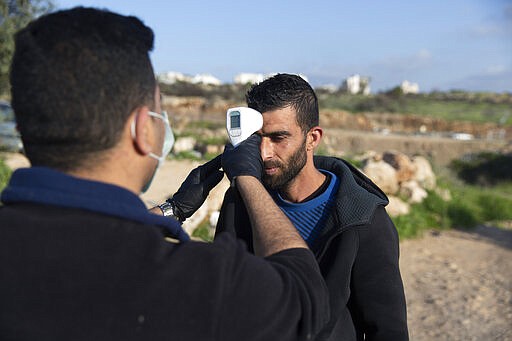 A paramedic from the Palestinian Ministry of Health checks the body temperature of a Palestinian laborer after exiting an Israeli army checkpoint, on his way home at the end of a day work in Israel, part of a strict precautionary measures to contain coronavirus outbreak, in the bordering West Bank village of Nilin, west of Ramallah, Wednesday, March 25, 2020. (AP Photo/Nasser Nasser)