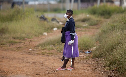 Noxolo Mbatha, wearing face masks and surgical gloves to protect herself against coronavirus, awaits a taxi for her hospital appointment at a informal settlement, east of Johannesburg, South Africa, Friday, March 27, 2020. The new coronavirus causes mild or moderate symptoms for most people, but for some, especially older adults and people with existing health problems, it can cause more severe illness or death. (AP Photo/Themba Hadebe)