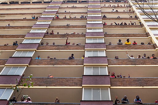 Residents of the densely populated Hillbrow neighborhood of downtown Johannesburg, confined in an attempt to prevent the spread coronavirus, stand and wave from their balconies, Friday, March 27, 2020. South Africa went into a nationwide lockdown for 21 days in an effort to mitigate the spread to the coronavirus. The new coronavirus causes mild or moderate symptoms for most people, but for some, especially older adults and people with existing health problems, it can cause more severe illness or death. (AP Photo/Jerome Delay)