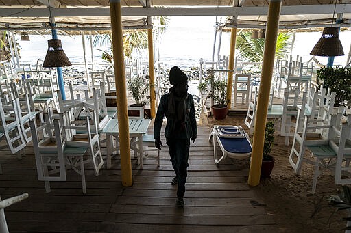 In this Thursday, March 26, 2020, photo, a security guard walks in a normally busy but now closed restaurant on a beach in Dakar, Senegal. As African countries have started shutting down borders and economic activity plummets, those who do informal work or run small businesses are suffering without the type of economic assistance that some countries in the developed world are able to provide. (AP Photo/Sylvain Cherkaoui)