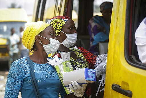 Women sell face masks and gloves, to prevent the spread of the new coronavirus, to passengers at a public minibus station in Lagos, Nigeria Friday, March 27, 2020. The new coronavirus causes mild or moderate symptoms for most people, but for some, especially older adults and people with existing health problems, it can cause more severe illness or death. (AP Photo/Sunday Alamba)