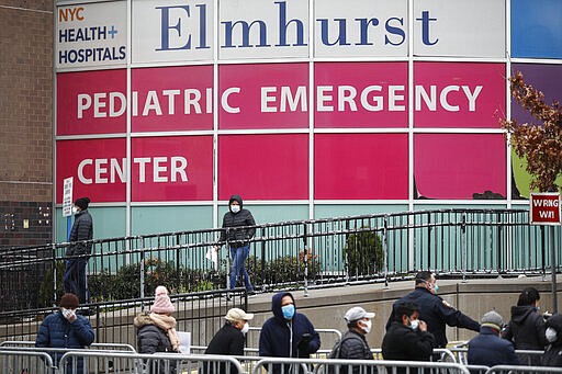 FILE - In this Wednesday, March 25, 2020, file photo, a woman exits a new coronavirus testing site while others wait in line at Elmhurst Hospital Center, in the Queens borough of New York. Los Angeles is half the size of New York City but has a disproportionately small fraction of the coronavirus cases and deaths as the nation's largest city. The same goes for California when compared with New York state as a whole, which is the current epicenter of the outbreak in the U.S. (AP Photo/John Minchillo, File)