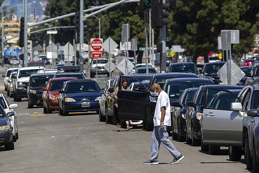 FILE - In this Wednesday, March 25, 2020, file photo, Los Angeles resident Larnell Brown, 66, wears gloves and a mask as he steps out of his waiting vehicle outside the Crenshaw Christian Center before it opens as a testing site for COVID-19 in South Los Angeles. Los Angeles is half the size of New York City but has a disproportionately small fraction of the coronavirus cases and deaths as the nation's largest city. The same goes for California when compared with New York state as a whole, which is the current epicenter of the outbreak in the U.S. (AP Photo/Damian Dovarganes, File)