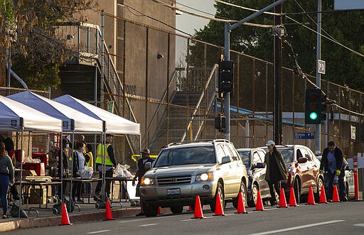 FILE - In this March 25, 2020, file photo, vehicles line up at a &quot;Grab &amp; Go&quot; stop to get free school meals provided by the Los Angeles Unified School District at the Virgil Middle School station Los Angeles. Los Angeles is half the size of New York City but has a disproportionately small fraction of the coronavirus cases and deaths as the nation's largest city. The same goes for California when compared with New York state as a whole, which is the current epicenter of the outbreak in the U.S. (AP Photo/Damian Dovarganes, File)