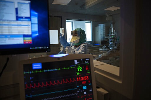 In this photograph taken from behind a window medical personnel work in the intensive care ward for Covid-19 patients at the MontLegia CHC hospital in Liege, Belgium, Friday, March 27, 2020. The new coronavirus causes mild or moderate symptoms for most people, but for some, especially older adults and people with existing health problems, it can cause more severe illness or death. (AP Photo/Francisco Seco)