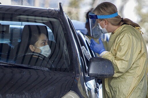 An Alberta Health Services employee speaks with a motorist at a drive-thru coronavirus testing facility in Calgary, Alberta, Friday, March 27, 2020. (Jeff McIntosh/The Canadian Press via AP)